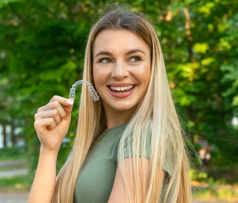 Smiling woman holding a clear aligner